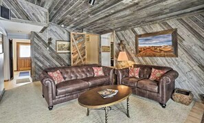 Una sala de estar rústica con un sofá seccional de cuero, una mesa de centro de madera y un cuadro con un paisaje en la pared.