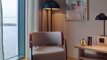 Ein modernes Zimmer mit Meerblick, ein Sessel, ein Schreibtisch mit Lampe und ein gerahmtes Bild an der Wand.