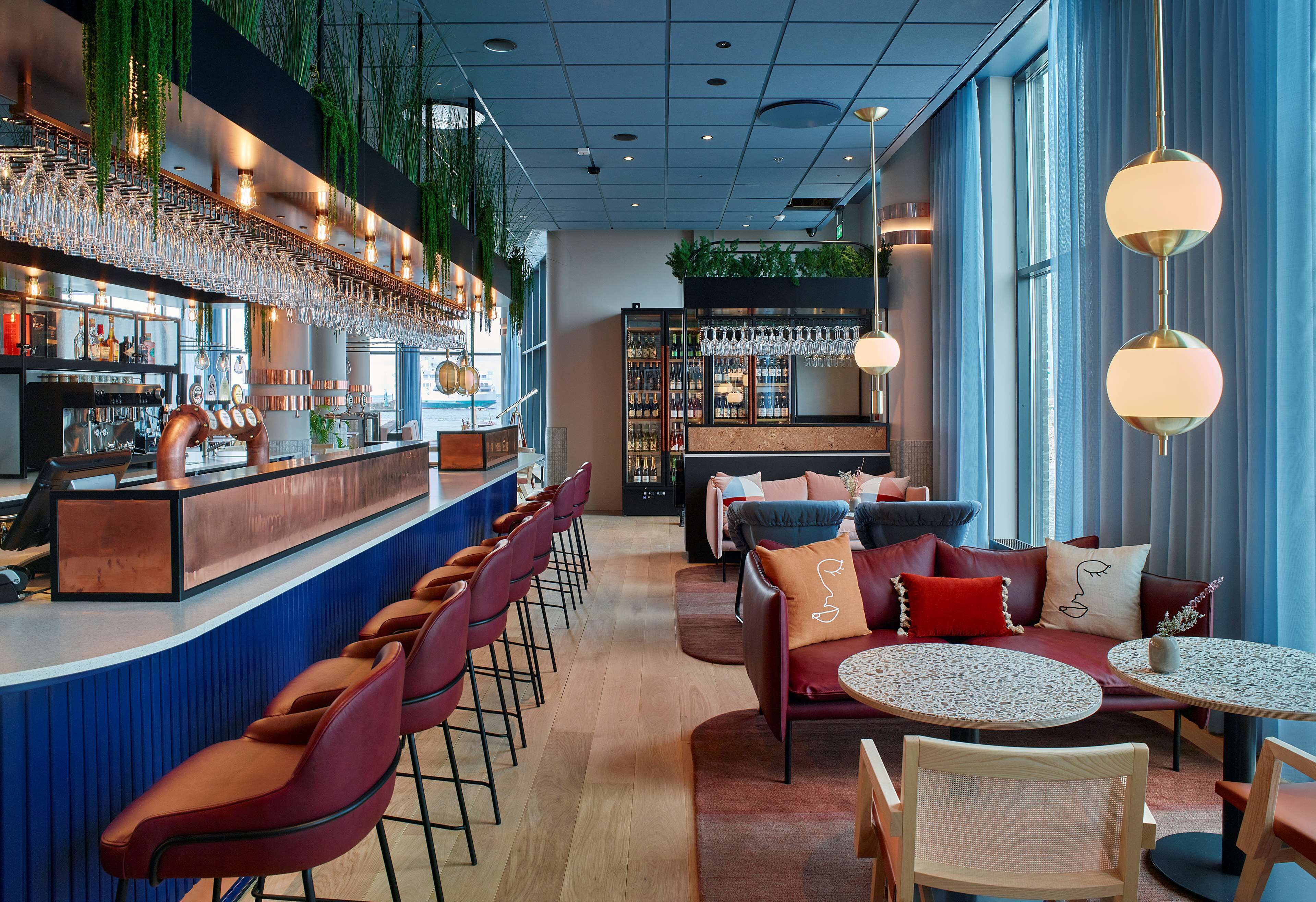 A bar area with stools, a counter, and a seating area with a sofa and round tables.