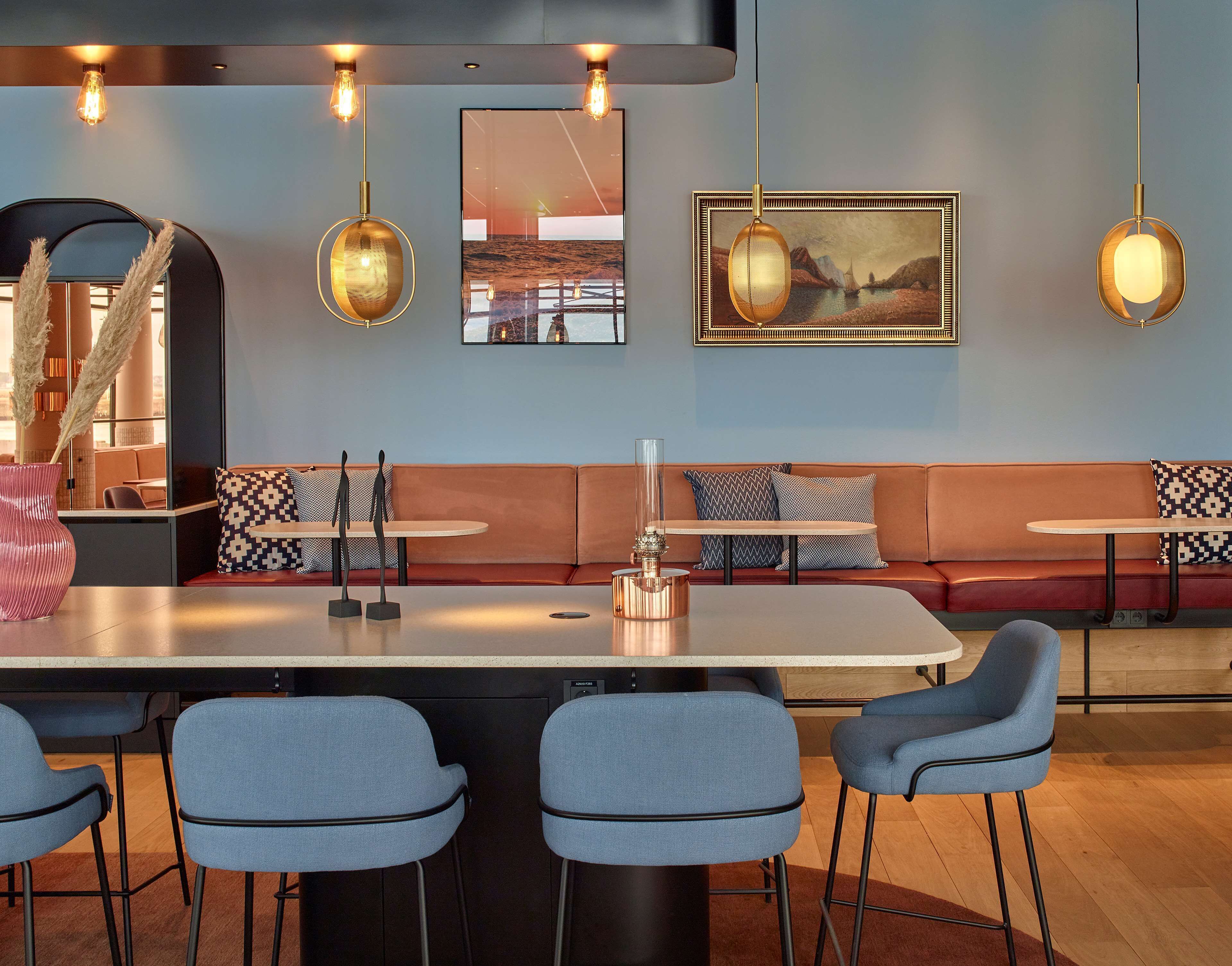 A modern restaurant interior with a central island, blue chairs, and a seating area with patterned cushions.