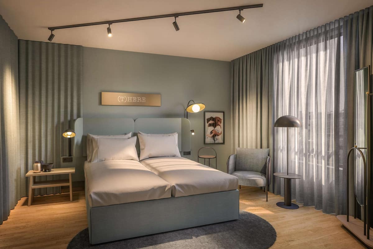 Un dormitorio moderno con cama, mesitas de noche, una silla, un escritorio y un ventanal con cortinas.
