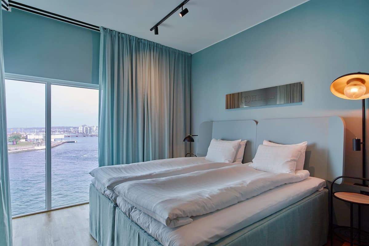 Habitación de hotel con una cama grande, un escritorio, una silla, una lámpara y vistas a una masa de agua.