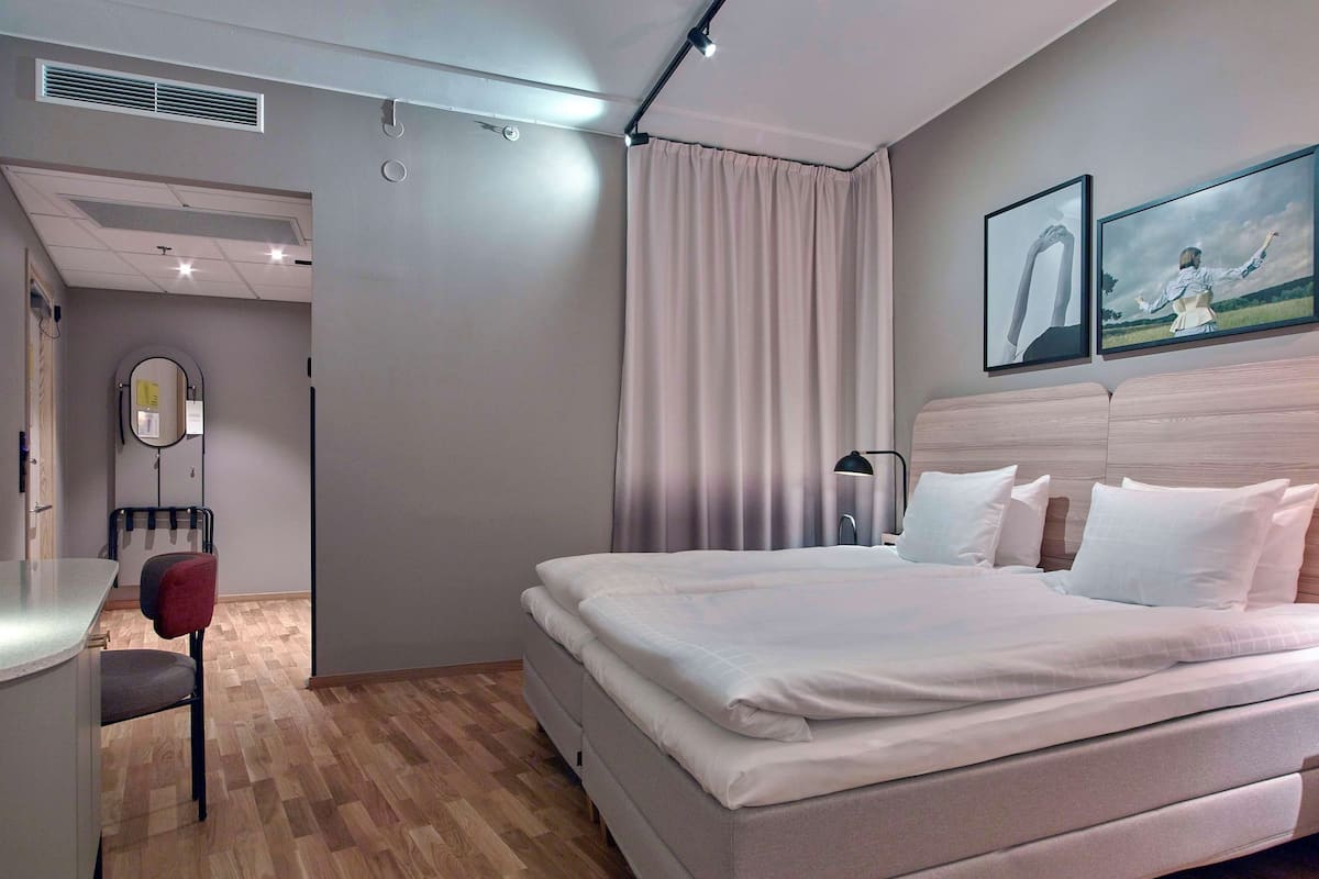 Una cama bien hecha con sábanas blancas, una lámpara de noche y dos cuadros en la pared.