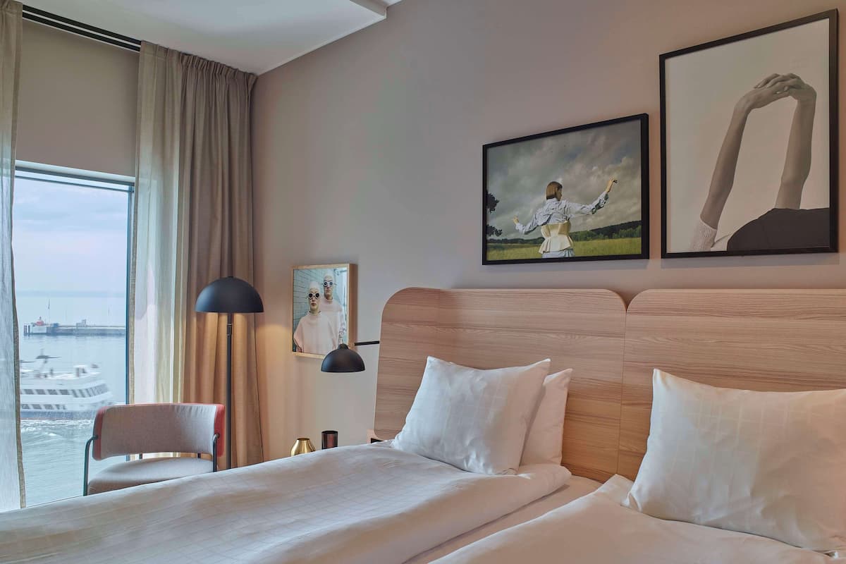 Una habitación de hotel con una cama grande, una silla, una lámpara y obras de arte en la pared.