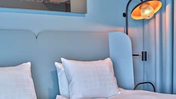 Un dormitorio con cama, almohadas, mesita de noche, lámpara de pared y espejo.