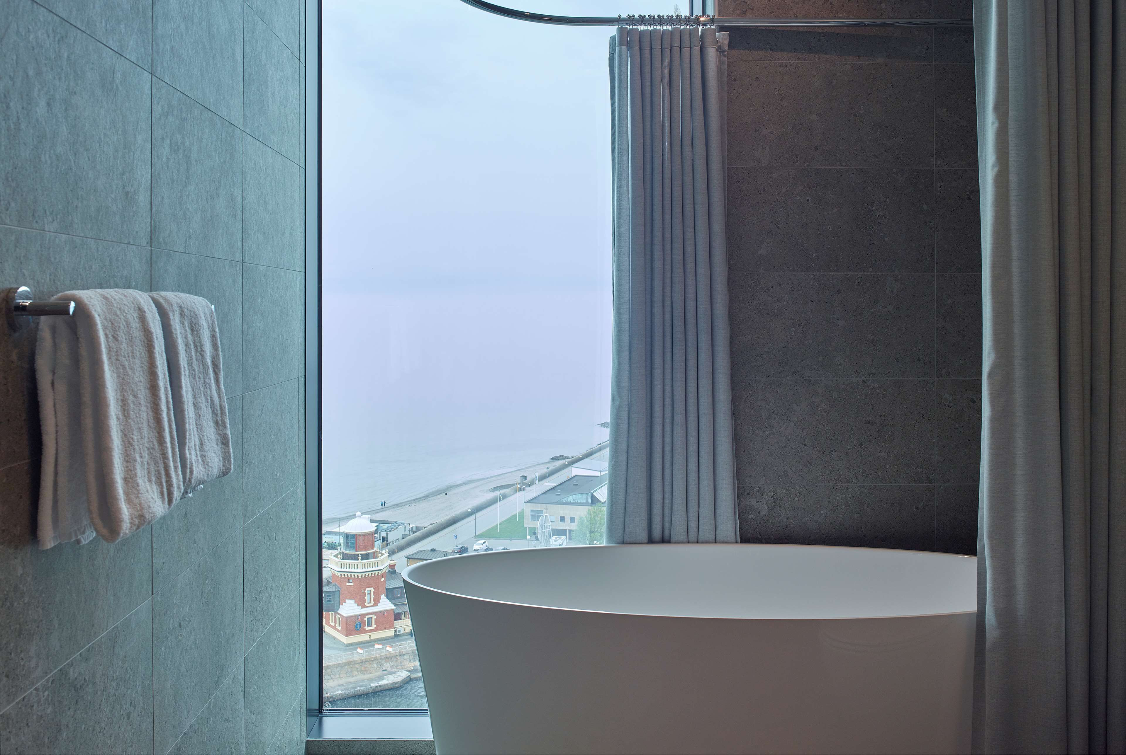 A bathroom with a bathtub, a towel rack, and a view of a building across the water.