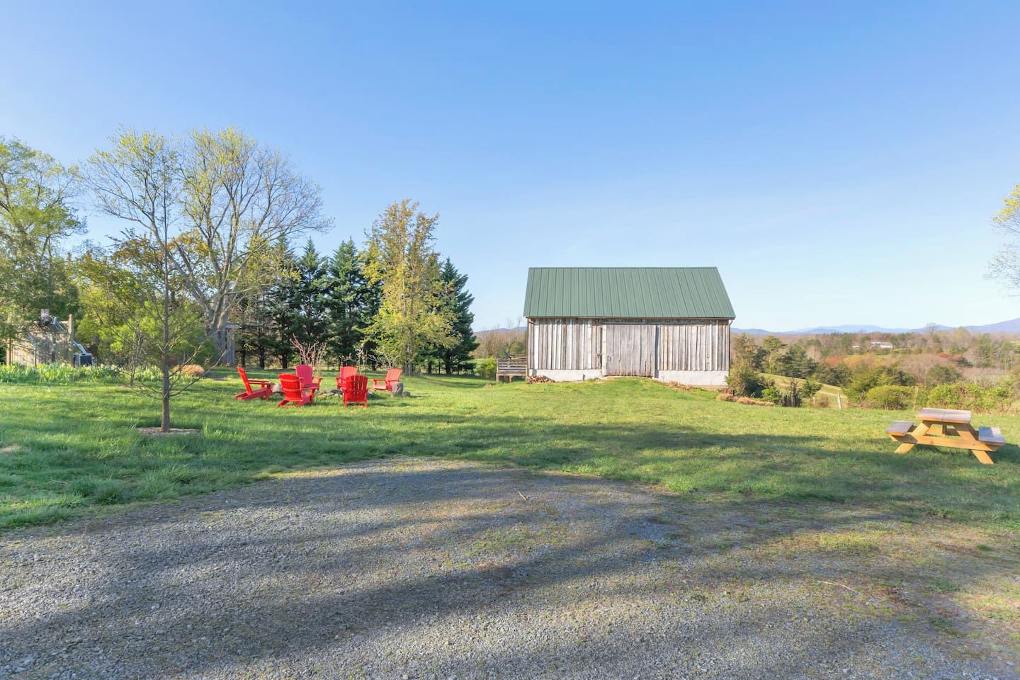 A rural landscape with a barn, red Adirondack chairs, and a picnic table.