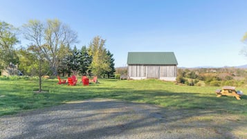 A rural landscape with a barn, red Adirondack chairs, and a picnic table.