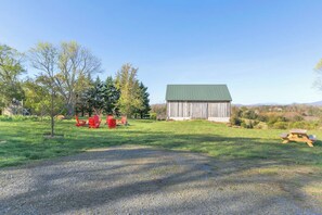 Paisagem rural com um celeiro, cadeiras Adirondack vermelhas e uma mesa de piquenique.