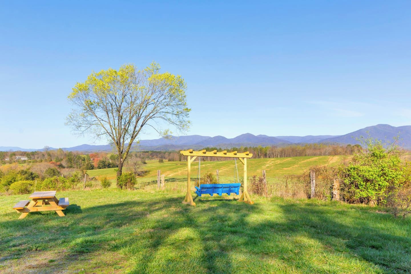 A grassy outdoor area with a wooden swing set and a picnic table.