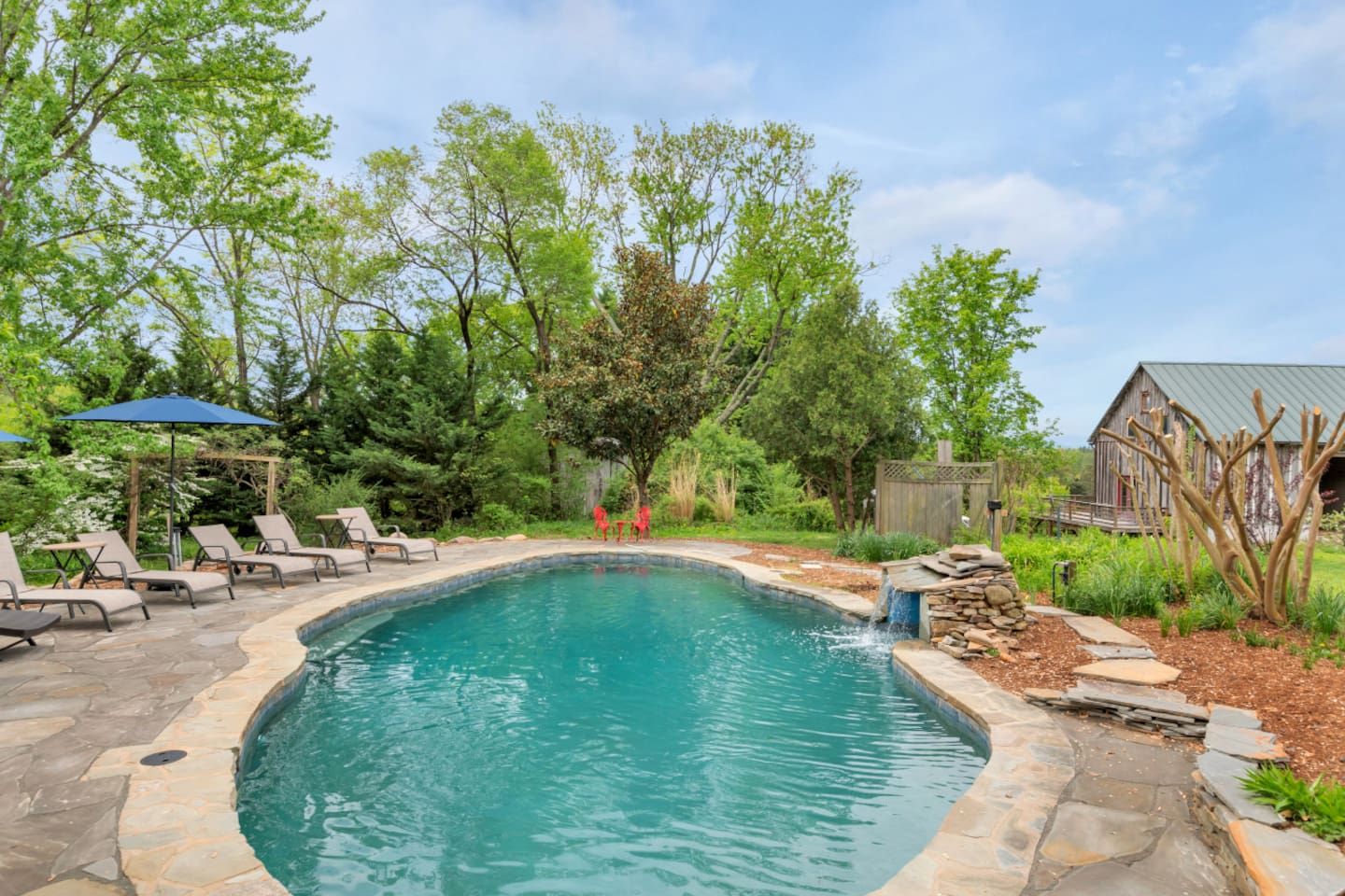 A swimming pool with a stone border, surrounded by lounge chairs and a wooden deck.
