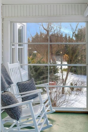 Un fauteuil à bascule avec des coussins à motifs, une fenêtre donnant sur un paysage enneigé et un plancher vert.