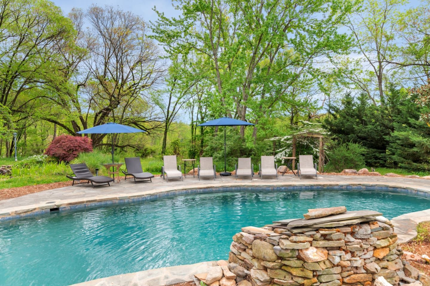 A swimming pool with lounge chairs and umbrellas, surrounded by trees and greenery.