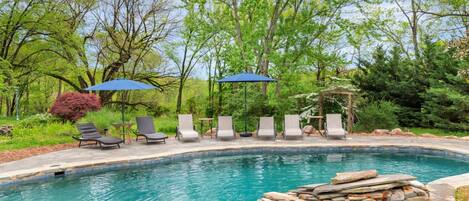 A swimming pool with lounge chairs and umbrellas, surrounded by trees and greenery.