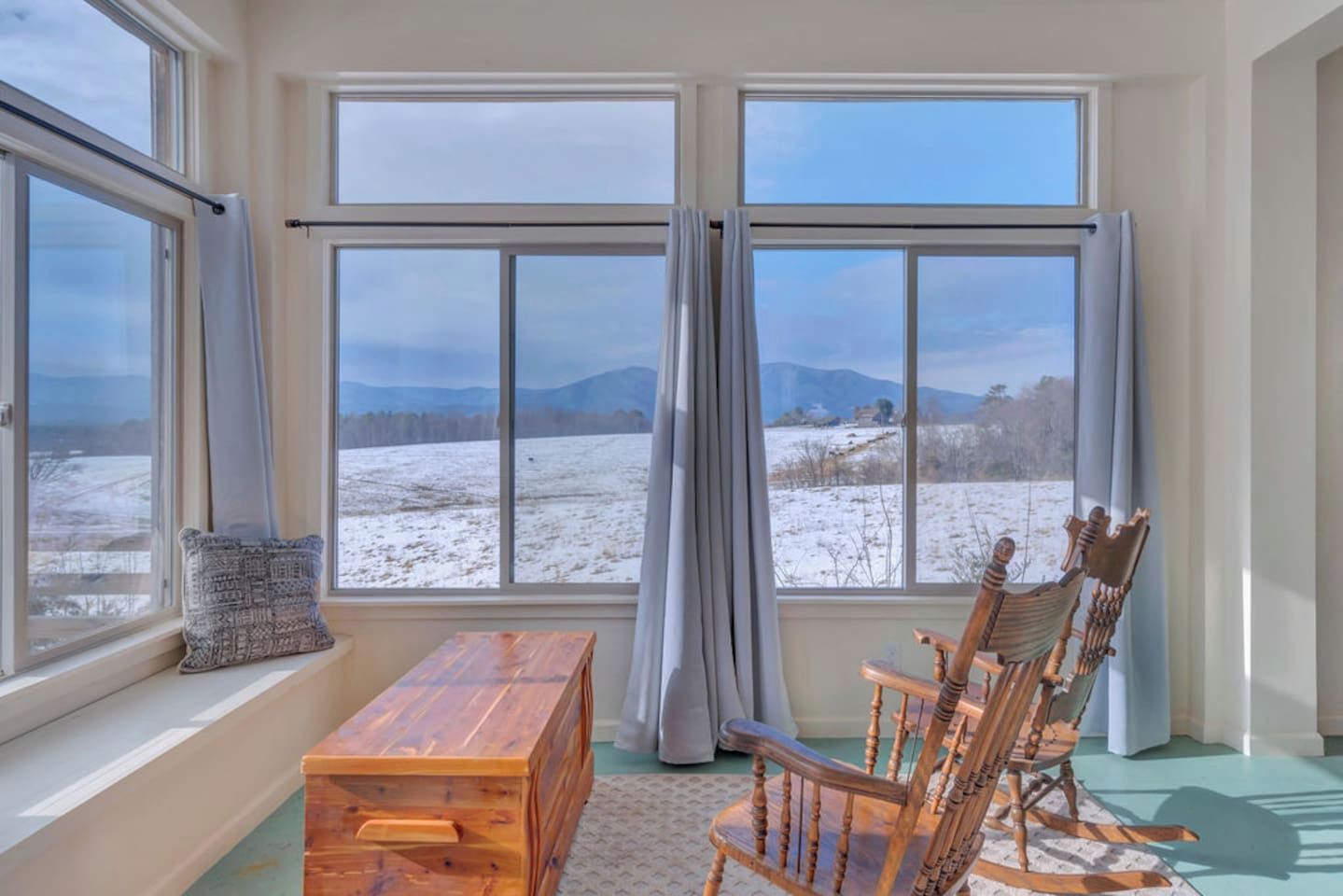 A room with large windows, a wooden bench, a rocking chair, and a view of a snowy landscape.