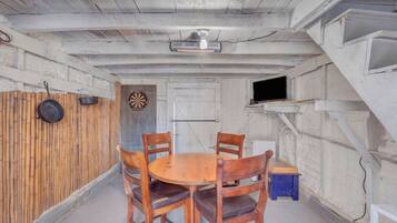 A room with a wooden table and chairs, a dartboard, a television on a shelf, and a door.
