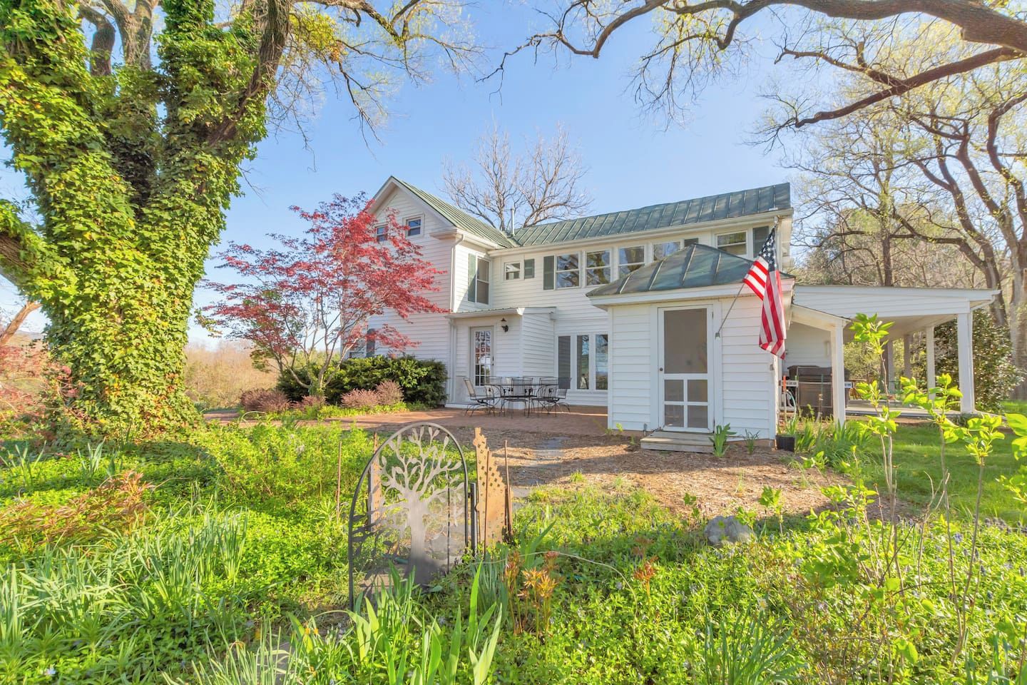 A two-story house with a porch, a flag, and a garden.