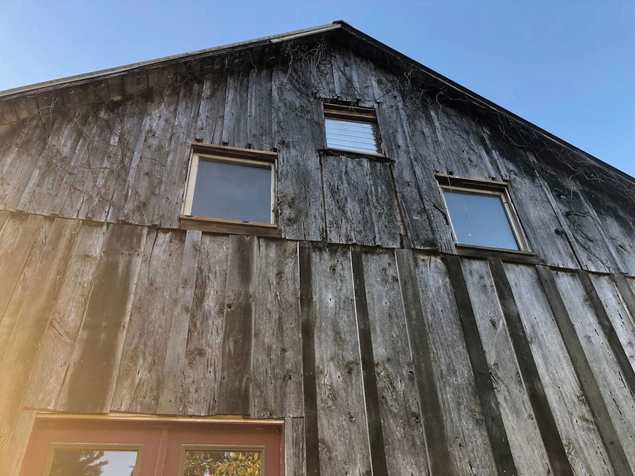 A rustic barn with a sloped roof, two small windows, and a red door.