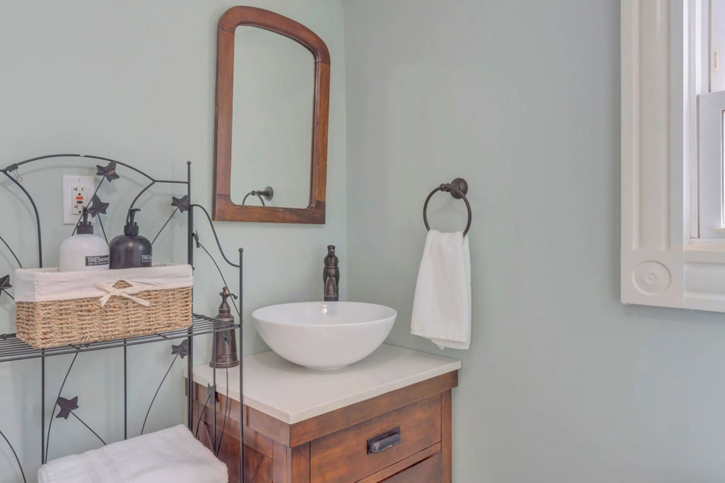 A bathroom with a white sink, a wooden vanity, a metal rack with toiletries, and a mirror.