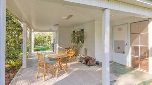 Een overdekt terras met een tafel, stoelen, een plant in pot en een schuifdeur van glas.