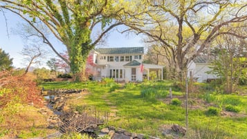 A two-story house with a covered porch, a stone pathway, and a small stream.