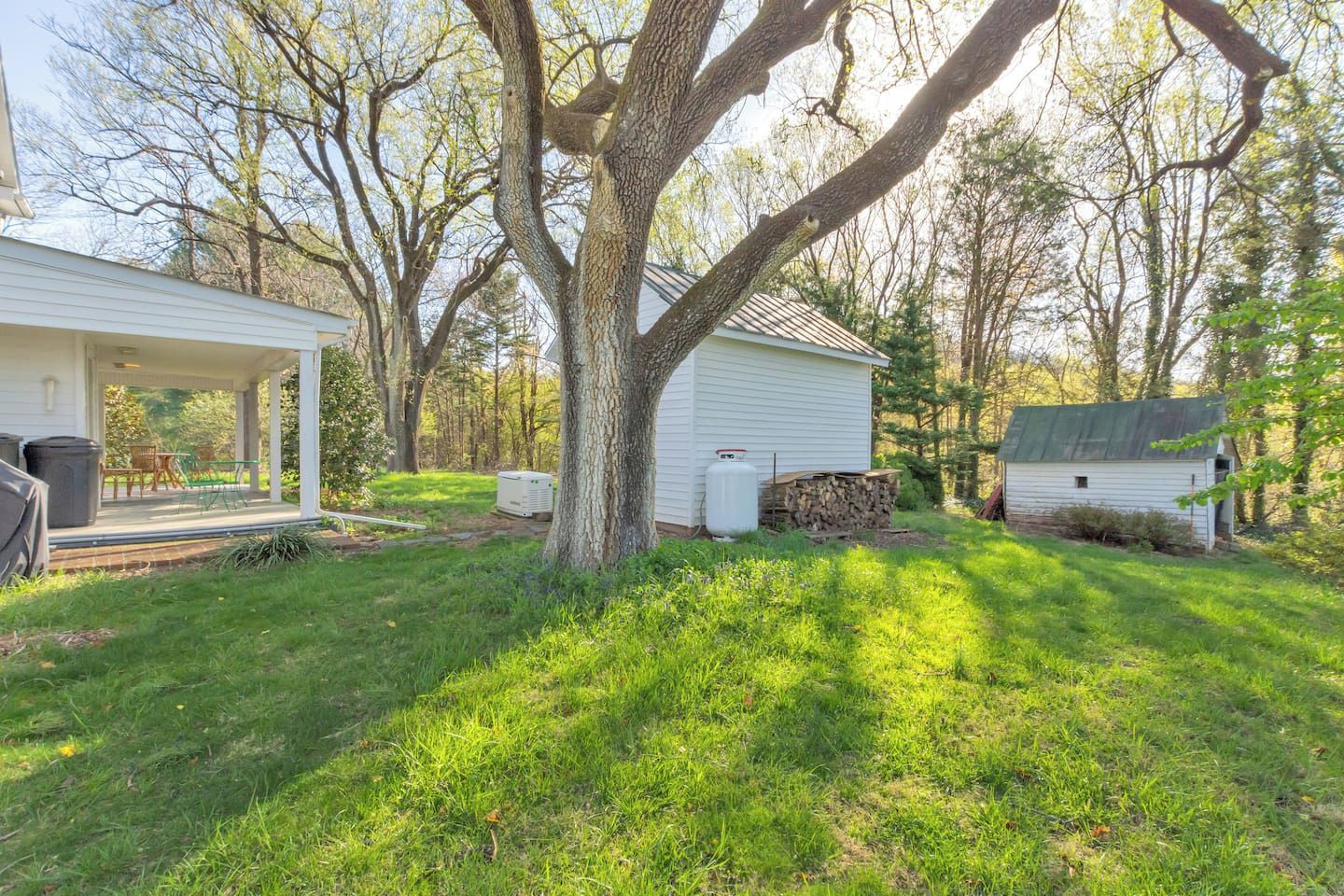 A residential property with a covered porch, a small shed, and a large tree.
