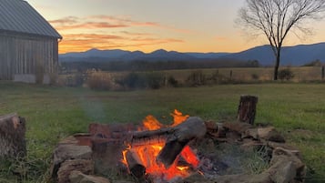 A campfire surrounded by rocks in a grassy field with mountains in the background.