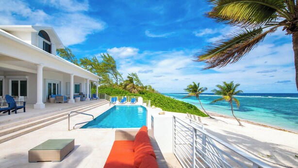 Ein Poolbereich mit Blick auf den Ozean, ein weißes Gebäude und ein rotes Sofa.