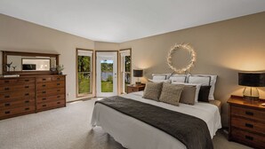 Un dormitorio con una cama grande, cómoda de madera y vistas a un jardín a través de una puerta corredera.
