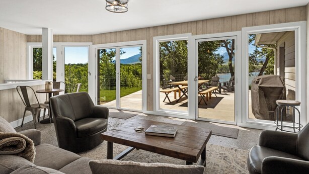 Amplia sala de estar con sofá, sillón y mesa de centro. Grandes puertas correderas de vidrio dan acceso a un patio exterior con mesa y sillas.