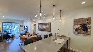 A modern kitchen with a large island, pendant lights, and a dining area with chairs and a table.