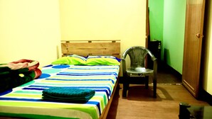 Un lit simple avec une couvre-lit à rayures, une chaise et une armoire en bois dans une pièce aux murs unis.