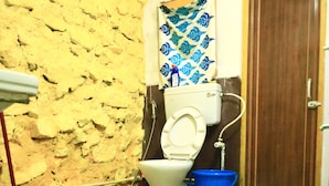 Une salle de bain avec des toilettes, un seau bleu, une serpillière et une porte.