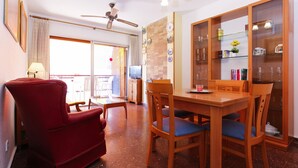 A dining area with a wooden table and chairs, a red armchair, a television, and a glass cabinet with decorative items. - PLAYAZUL 2 Apartment (Cambrils)