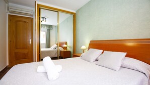 A hotel room with a large bed, a wooden headboard, a mirror, a wardrobe, and a bedside table with a lamp. - PLAYAZUL 2 Apartment (Cambrils)