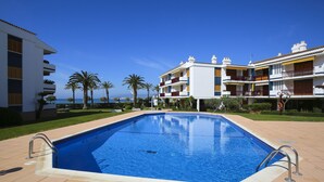 A swimming pool with a tiled deck, surrounded by palm trees and a building with multiple balconies. - PLAYAZUL 2 Apartment (Cambrils)