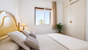 Quarto com cama, mesa de cabeceira, luminária, janela com cortinas, planta e guarda-roupa.