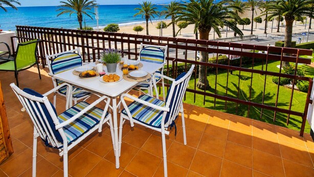 Varanda com mesa posta para o café da manhã, com vista para uma praia e palmeiras.