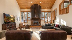 A spacious living room with a fireplace, leather sofas, a large TV, and a wooden ceiling. - Grand Antler Lodge: Spacious, Updated, Sleeps 16 (Breckenridge)