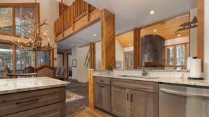 A spacious kitchen with wooden cabinets, a granite countertop, and a large window overlooking a forest. - Grand Antler Lodge: Spacious, Updated, Sleeps 16 (Breckenridge)