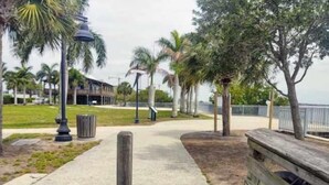 A paved walkway with wooden posts, palm trees, and a building in the background. - Newly Renovated Charlotte Harbor - Sunset Inn #5 (Port Charlotte)