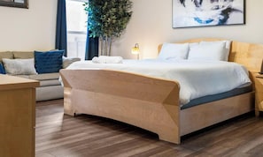 Un dormitorio moderno con una cama de madera, un sofá, una mesita de noche y un ventanal grande.