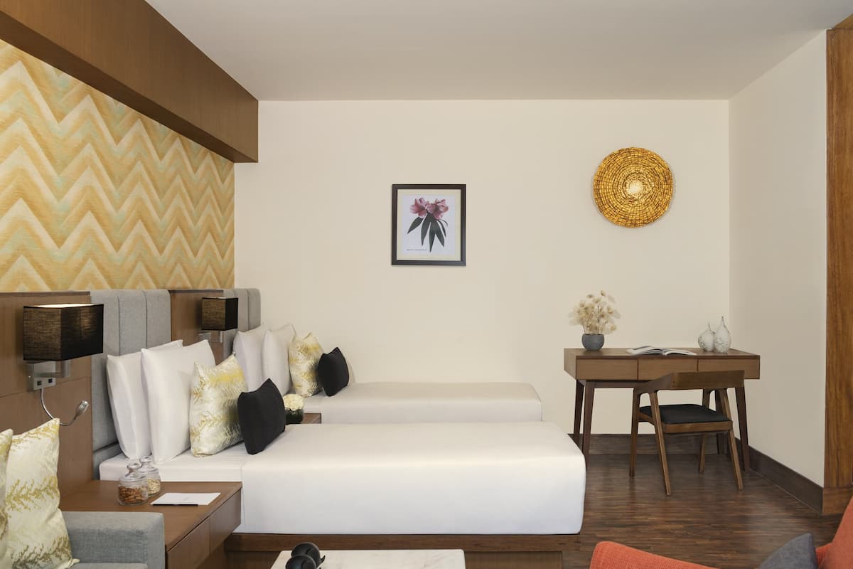 A modern hotel room with a bed, a desk, and a chair. There is a wall with a chevron pattern and a framed picture of a flower.