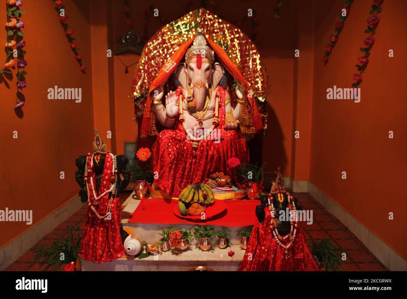 A statue of a deity with a red cloth, surrounded by offerings and flowers.