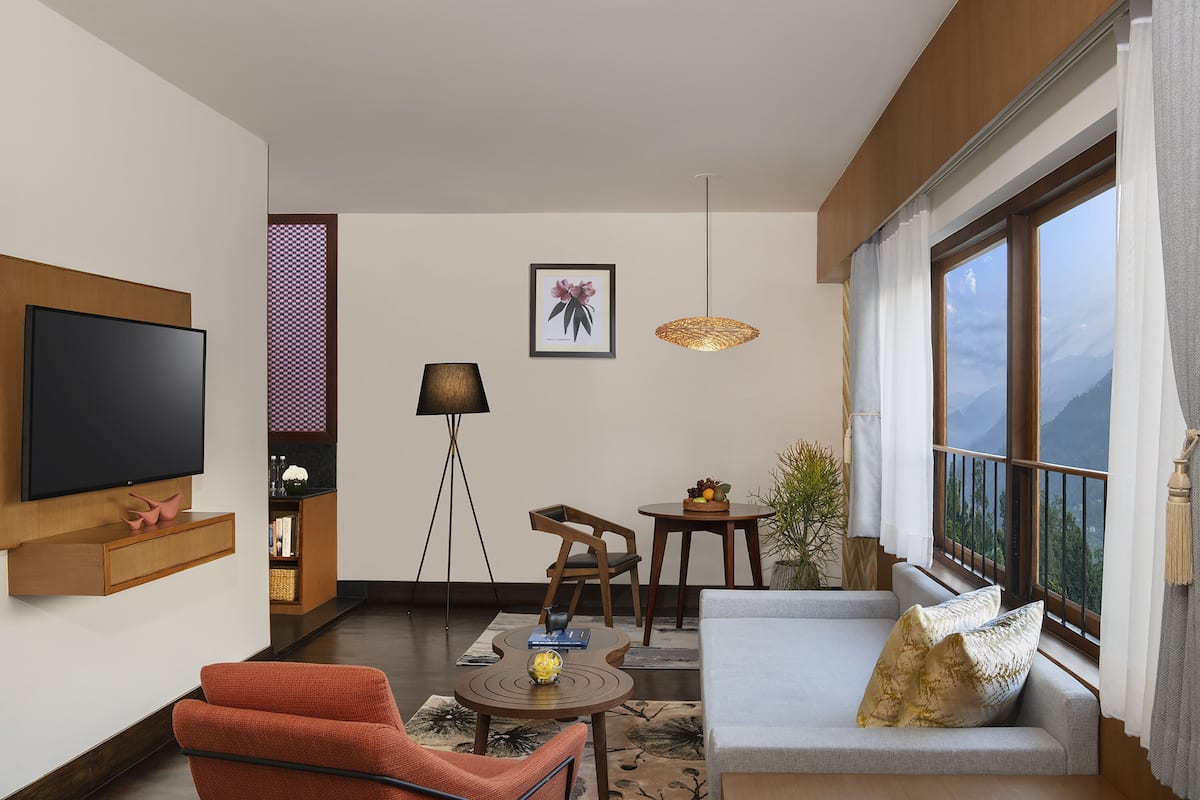 A modern living room with a TV, sofa, chairs, a small table, and a view of mountains.