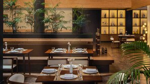 Restaurante com teto e paredes de madeira, mesas preparadas para refeições e prateleiras decorativas.