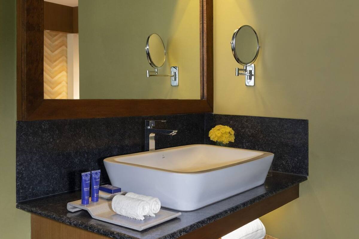 A bathroom with a large mirror, a vessel sink, a towel rack, and a small basket.