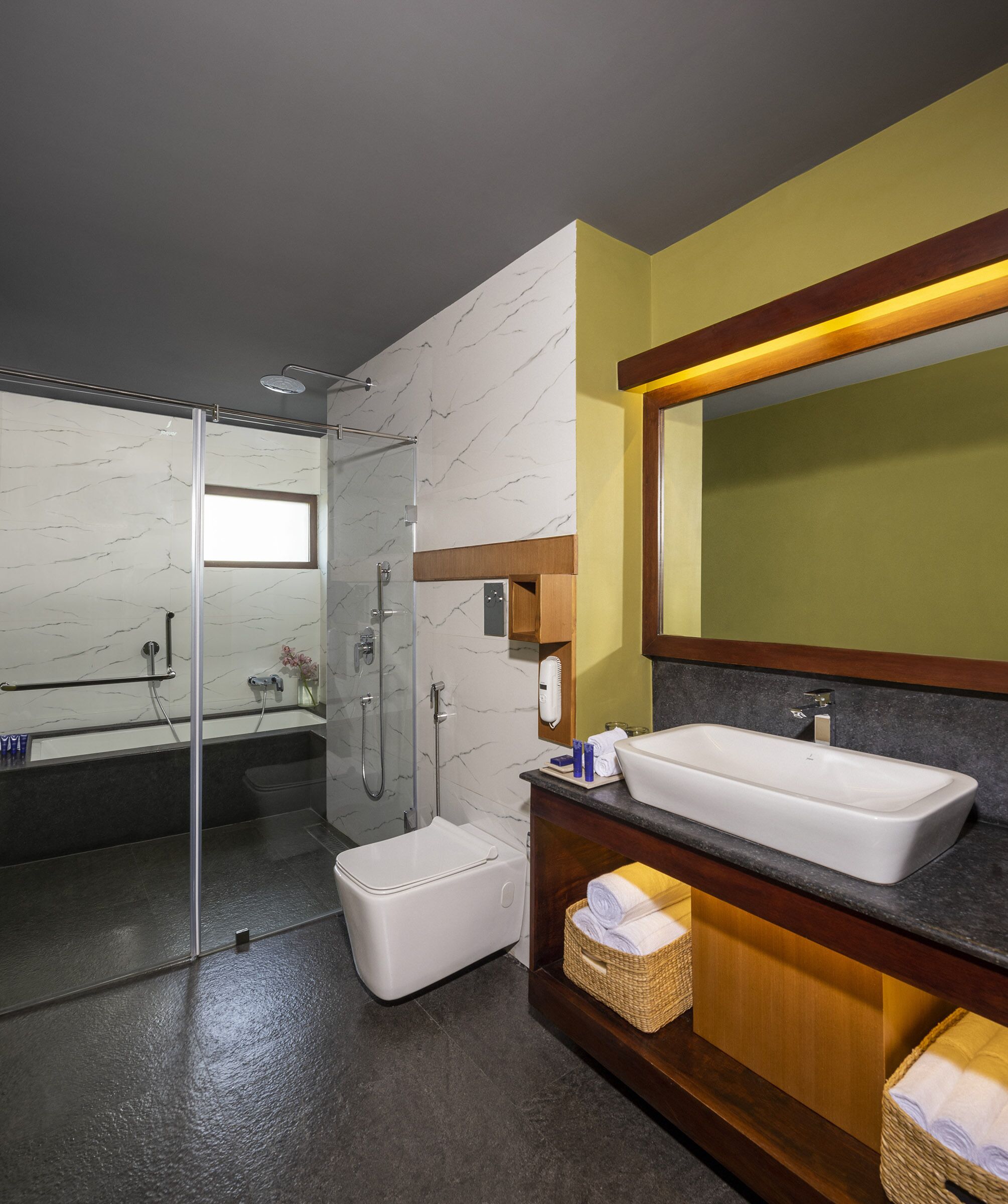 Un baño moderno con ducha envuelta en vidrio, un lavamanos blanco y un mueble de tocador de madera.