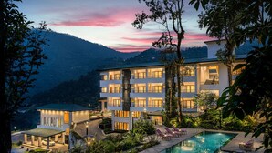 Um hotel com piscina, rodeado por vegetação exuberante e um cenário montanhoso.