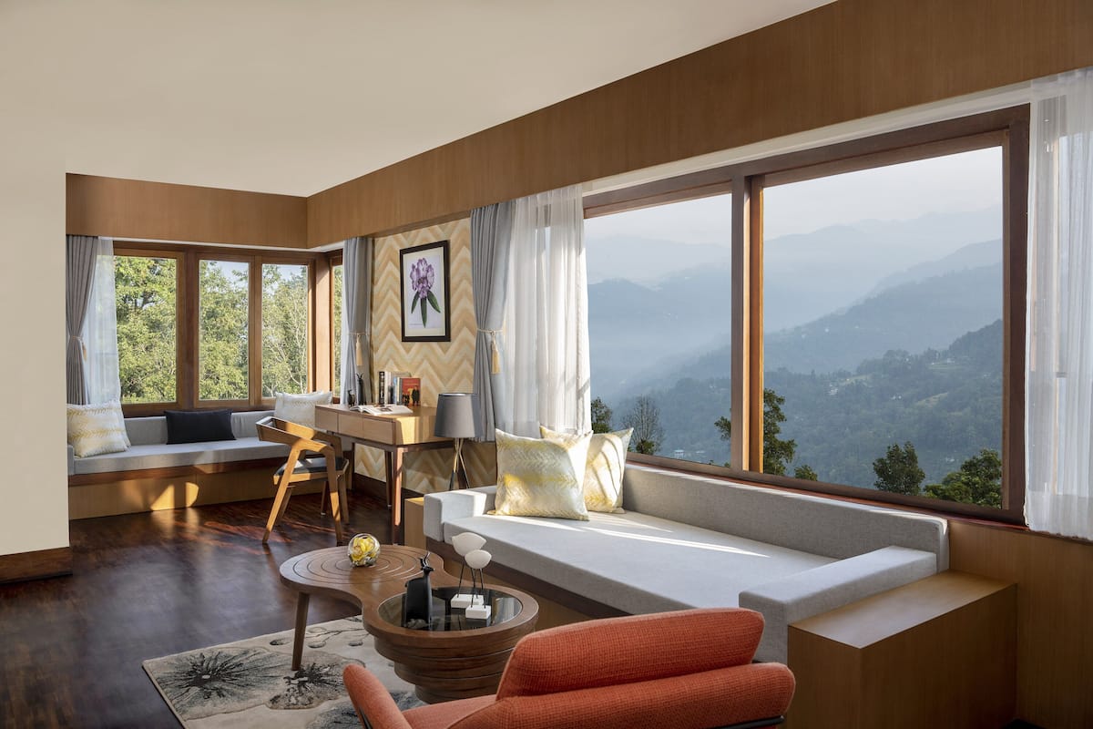 A modern living room with a large window, a sofa, a dining area, and a view of the mountains.
